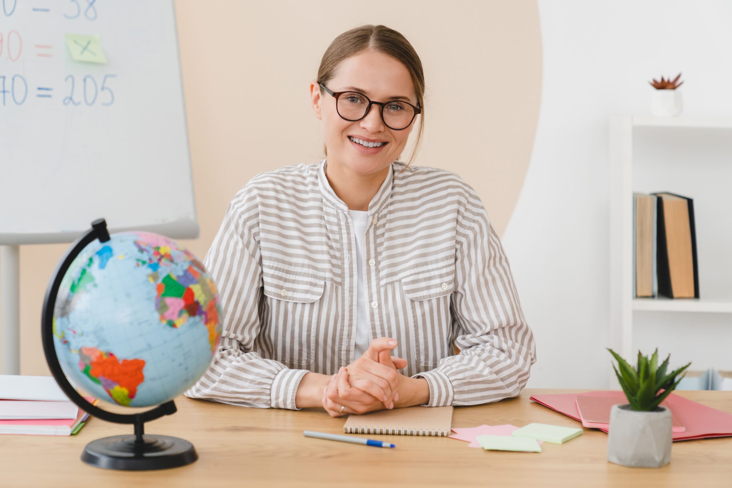 Una mujer sentada con un globo terráqueo en su mesa y una pizarra detrás